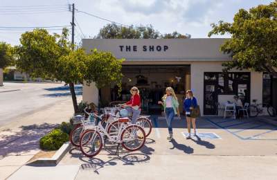 Three women walking to bikes parked outside of a building called "The Shop"