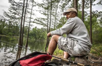 Man fishing along the shoreline at Carvers Creek State Park, surrounded by pine trees and calm water.