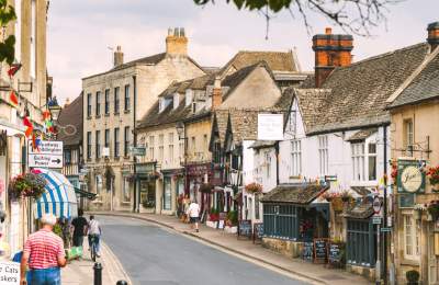 People walking and cycling along the High Street, which is decorated with flowering baskets and bunting, in Winchcombe in the Cotswolds