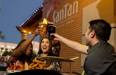 Two women and one man cheers beers on SanTan Brewing patio with food.