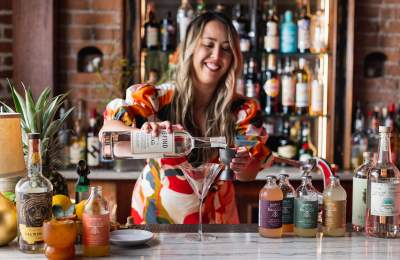 Women pouring vodka into a jigger with a glass and mixers on the bar