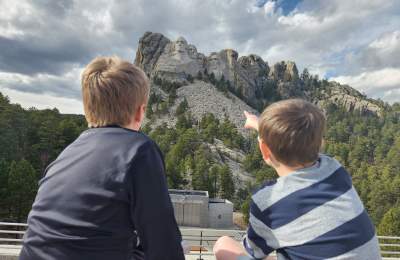two kids sitting on the grand view terrace at mount rushmore pointing at the memorial