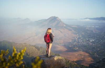 Solo hiker with red backpack looking out from mountain top