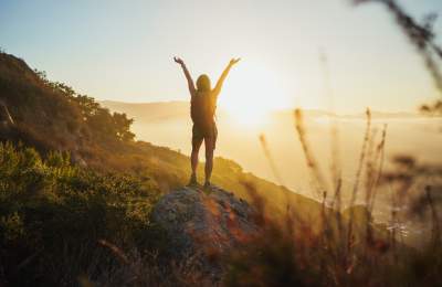 Hiker on a rock enjoying sunrise with hands up