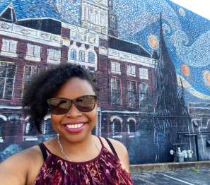 lady smiling in front of a large mural