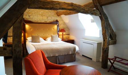 A large bed with gold upholstered headboard is framed by original wooden beams