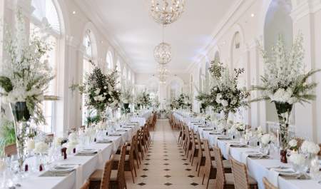 Long tables stretch the length of the Orangery at Blenheim Palace, decorated with white linen, place settings and large vases of white flower arrangements