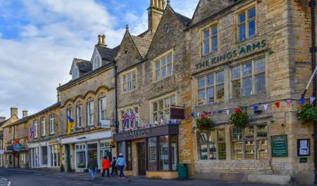 A family walking past shops of honey-coloured Cotswold stone in Stow on the Wold, in the Cotswolds