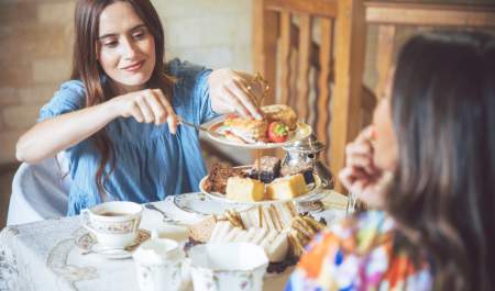 A woman in a blue dress takes a scone from a cake stand, which is filled with sandwiches, scones and cakes, in the Cotswolds