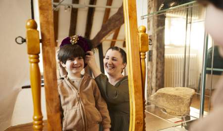 Mother and son standing in front on mirror playing dress up at Tudor House and Garden