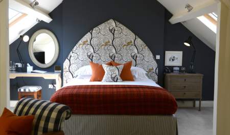 Bedroom at The Close Hotel in Tetbury with dark blue wall and elaborate headboard