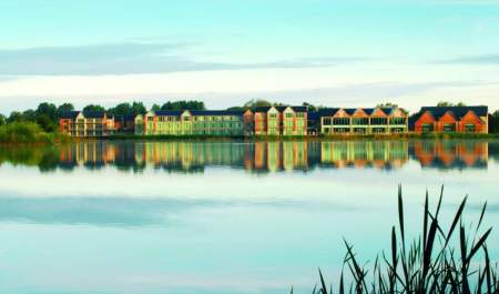A Cotswold lake ripples in the breeze, in the distance the De Vere Cotswold Water Park stands on the lakeside