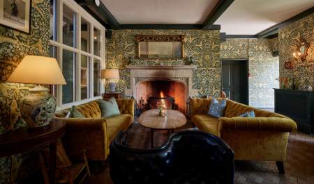 Ochre-coloured velvet sofas sit by a lit fire creating a warm and inviting lounge at The Old Bell Hotel in the Cotswolds