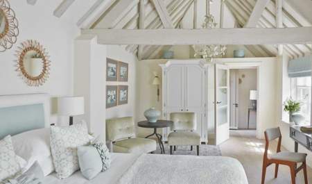 A light and airy bedroom with white washed rafters over a large bed with cosy blanket and pillows