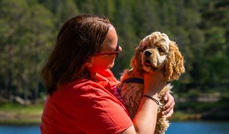 Dame som sitter med hunden på fanget ved ett tjern