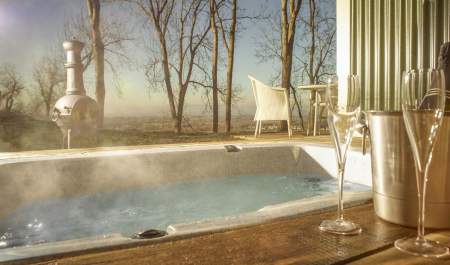 A bottle of champagne chills next to a hot tub with a breathtaking view of rolling hills at the Hilly Huts at the Fish Hotel in the Cotswolds