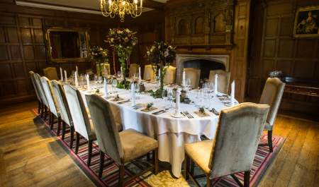 A large oval table decorated with flower arrangements in the middle of a wood panelled room with a large chandalier hanging from the ceiling