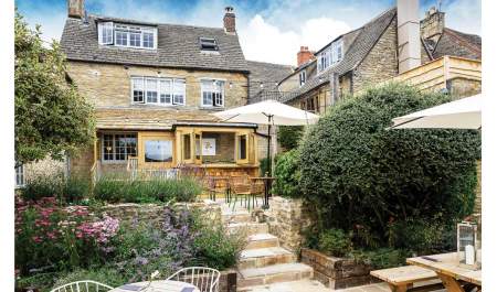 Stone steps lead from the patio through flower borders to the rear façade of The Old Stocks Inn in the Cotswolds