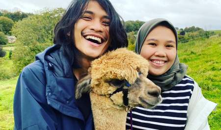 Two people smiling and posing with an alpaca