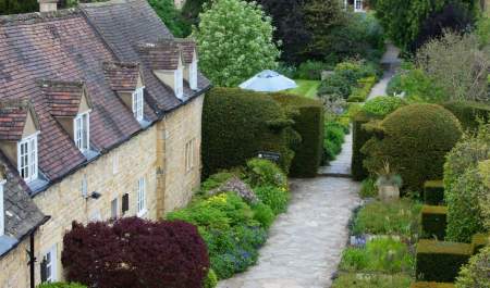 A birds-eye view, a grey stone path meanders through flower borders alongside a Cotswold stone building at the Cotswold House Hotel & Spa in the Cotswolds