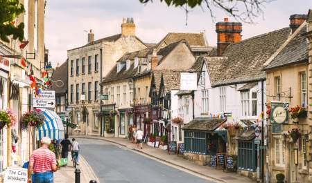 People walking and cycling along the High Street, which is decorated with flowering baskets and bunting, in Winchcombe in the Cotswolds