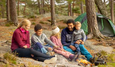 Familie på tur i skogen hvor de griller pølser.
