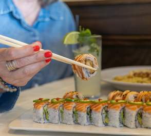 Hand with chopsticks holding a piece of sushi above a plate full of sushi at Barolo Grille in Salina, Kansas