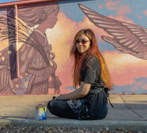 Amy Sol sits in front of her mural