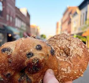 hand holding two bagles in a downtown street