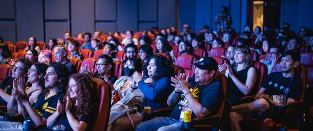 People sitting in theater seats clapping.