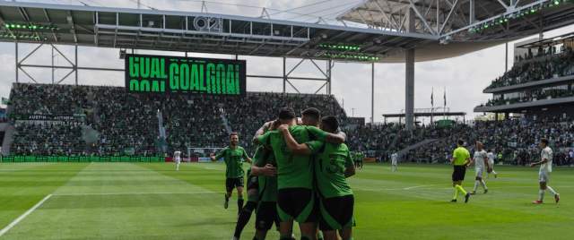 Image of some Austin FC players huddling on the field at Q2 Stadium during a game.