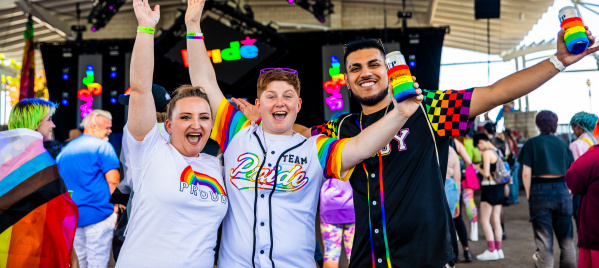 three friends cheering in front of a stage at pridefest