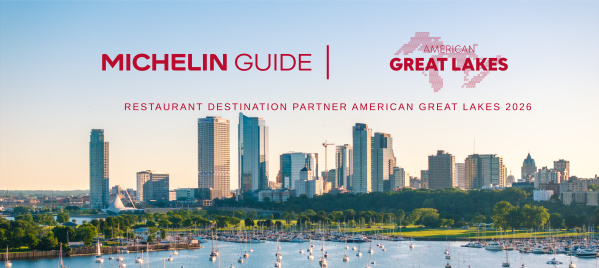 A waterfront view of Milwaukee’s skyline at sunset, with sailboats docked in the marina and a tour boat moving across Lake Michigan in the foreground. Above the skyline, red text reads “Michelin Guide | American Great Lakes” with the subheading “Restaurant Destination Partner American Great Lakes 2026.”