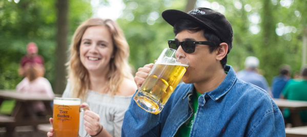 Two people at Hubbard Park Beer Garden, drinking beer over a large hot pretzel.