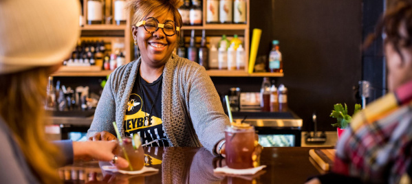 A bartender serving a non-alcoholic cocktail to two bar patrons.