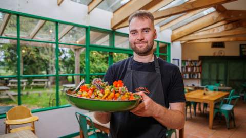 A chef holds a large dish of food in the cafe at The Organic Farm Shop & Cafe, Abbey Home Farm
