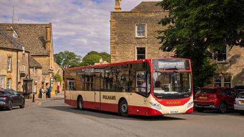 The single-decker Pulham's 801 bus driving along a street with honey-coloured buildings in Stow on the Wold