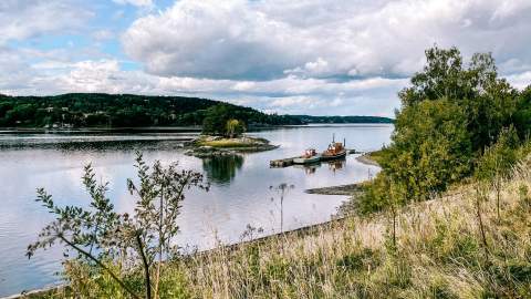 Utsikt over Glomma fra Furuholmen. To gamle båter ligger til kai langs ei flytebrygge.