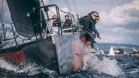 Menn som sitter på kanten av en seilbåt i full fart