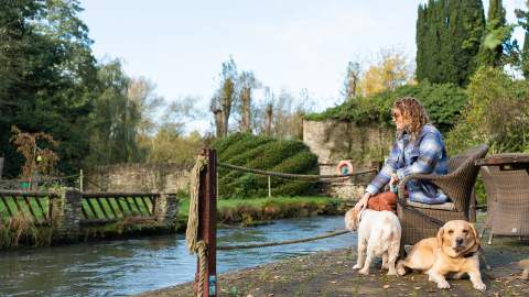 Woman with two dogs sat on a bench by the river at Minster Mill
