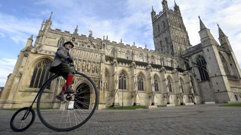 Man on a penny farthing bicycle in front of Gloucester Cathedral