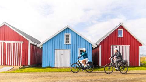 En mann og en kvinne på sykkel foran båthus i Farsund