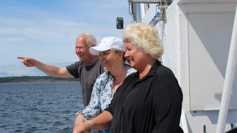 En mann og to kvinner står ved relingen på en båt og peker ut mot havet