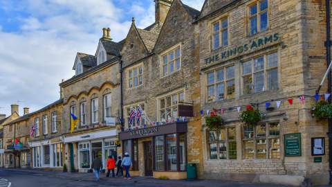 A family walking past shops of honey-coloured Cotswold stone in Stow on the Wold, in the Cotswolds