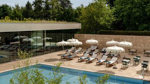 An outdoor swimming pool with rows of sunbeds and sun umbrellas, surrounded by trees at Cowley Manor, in the Cotswolds