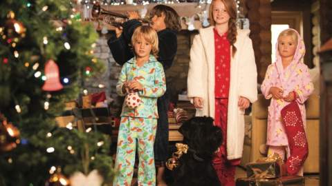 A group of children in pyjamas and their black dog stand in front of a Christmas tree at Log House Holidays