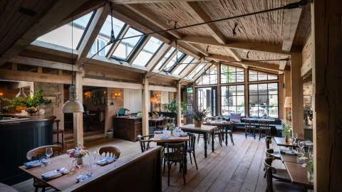A large wooden conservatory with tables dressed for dinner with fresh flowers at Royal Oak Ramsden in the Cotswolds