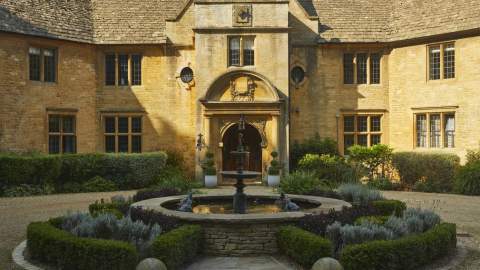 A circular fountain surrounded by topiary creates a stunning centrepiece in front of the entrance to the impressive honey-coloured stone Foxhill Manor