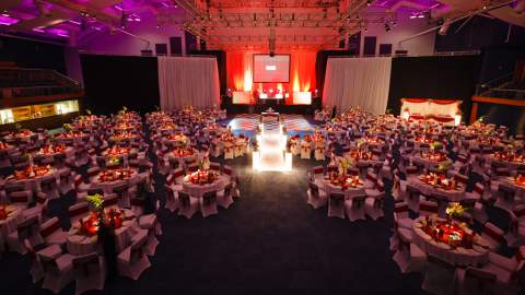 A large room with stage and large screen, and tables dressed for a gala dinner at Cheltenham Racecourse
