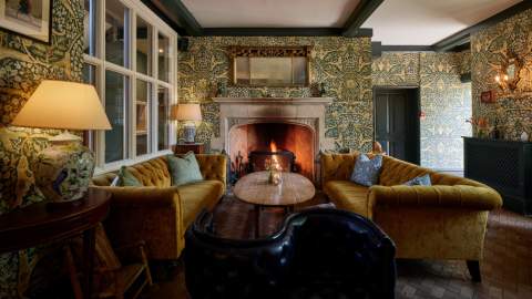 Ochre-coloured velvet sofas sit by a lit fire creating a warm and inviting lounge at The Old Bell Hotel in the Cotswolds